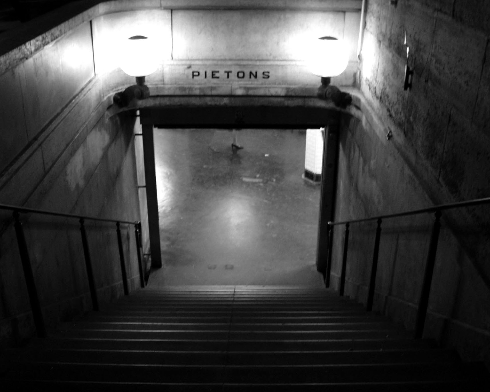Stairs descending to an underpass lit by two globe lamps, sign reading Piétons