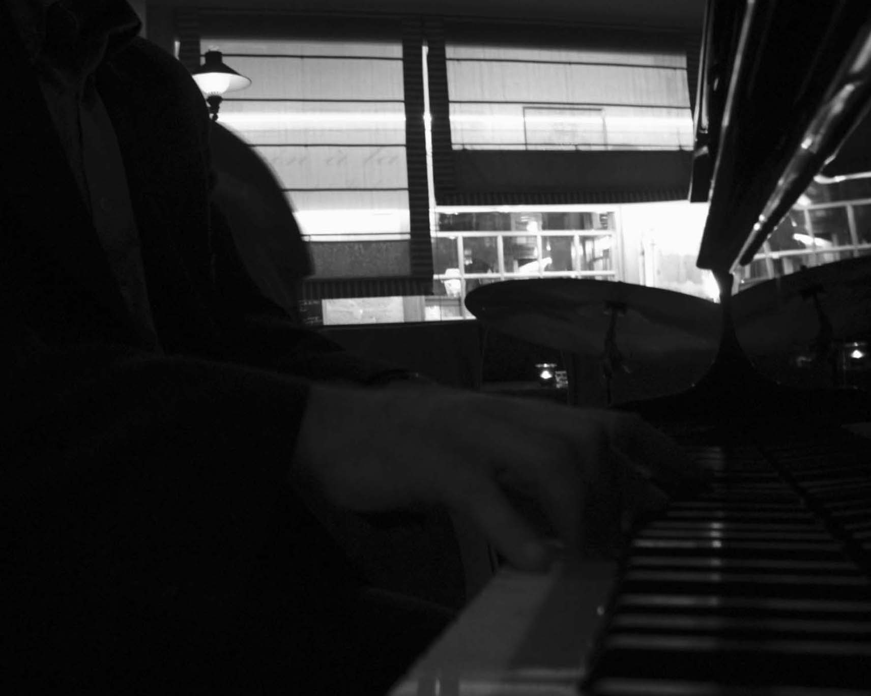 Hands on piano keys, cymbals and a lit window behind