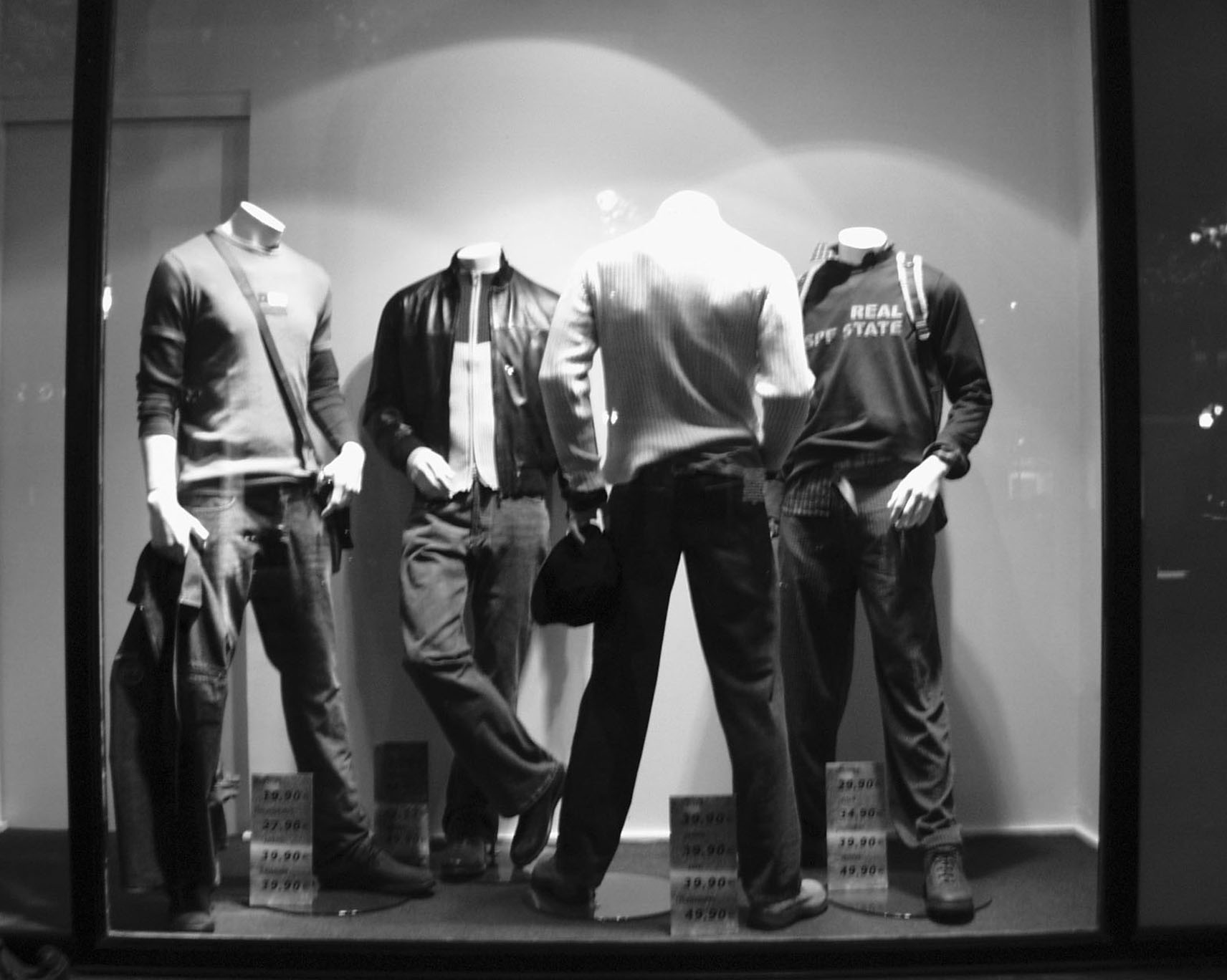 Four headless mannequins in casual clothes in a lit shop window