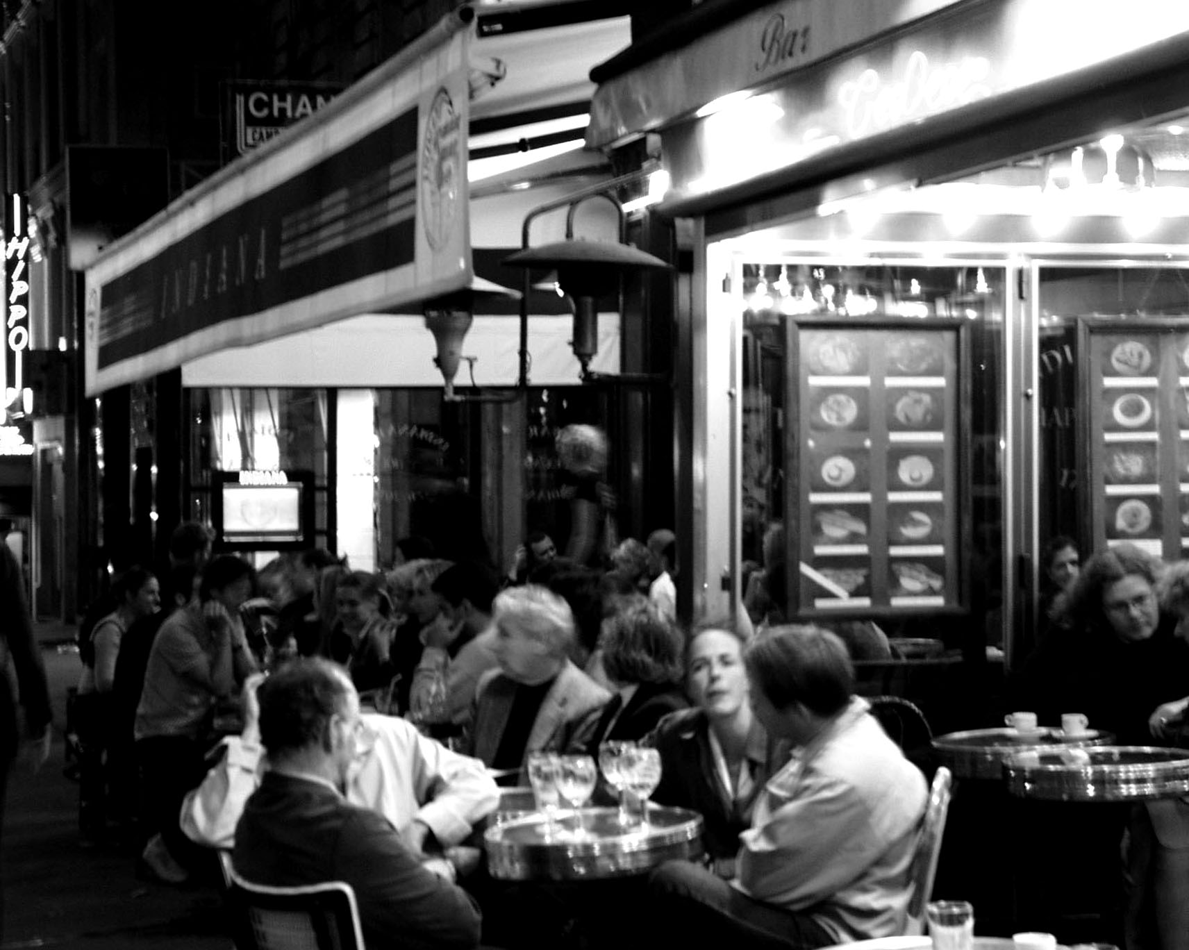 Crowded café terrace at night under an awning reading Indiana
