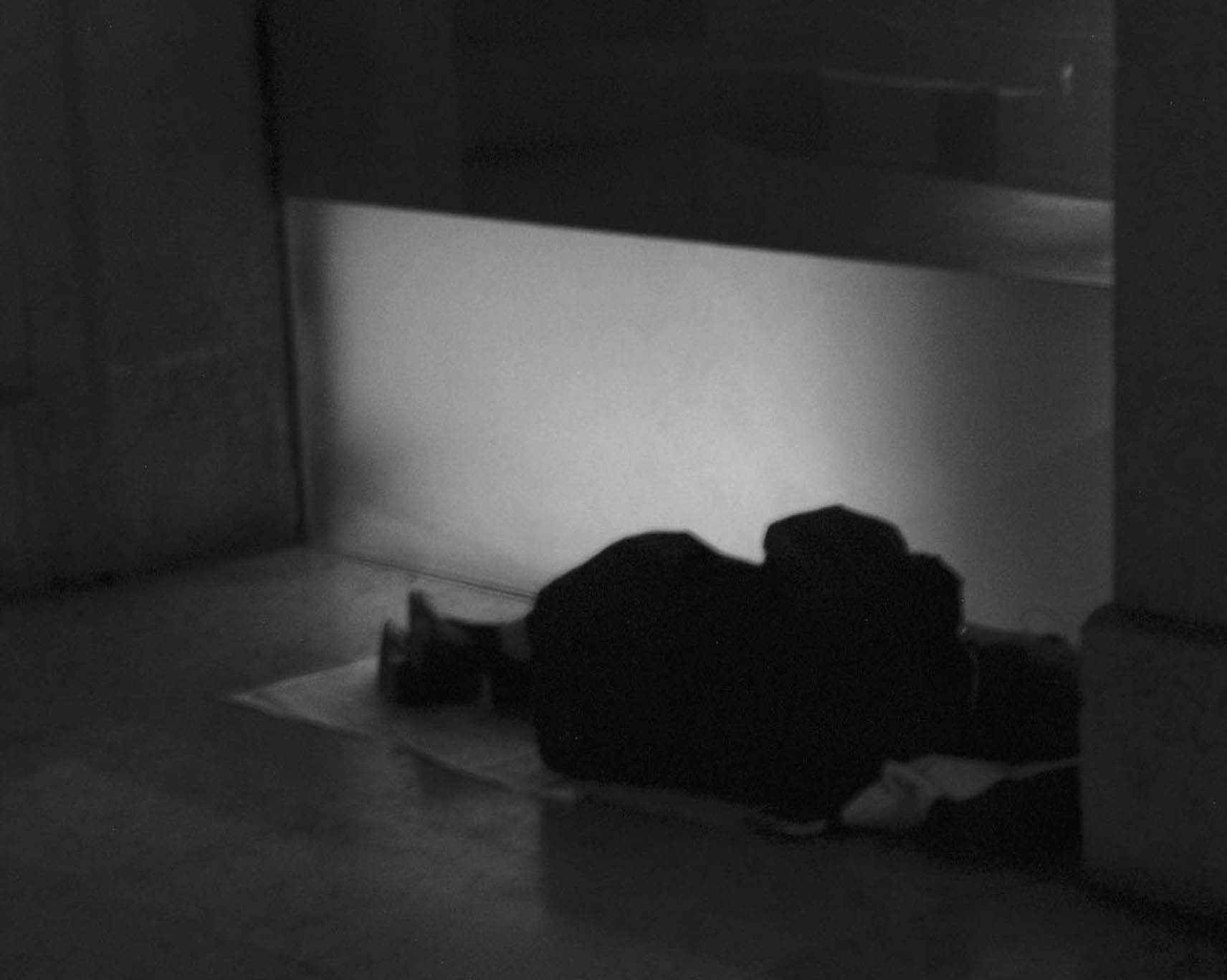 A figure sleeping on the floor against a lit wall