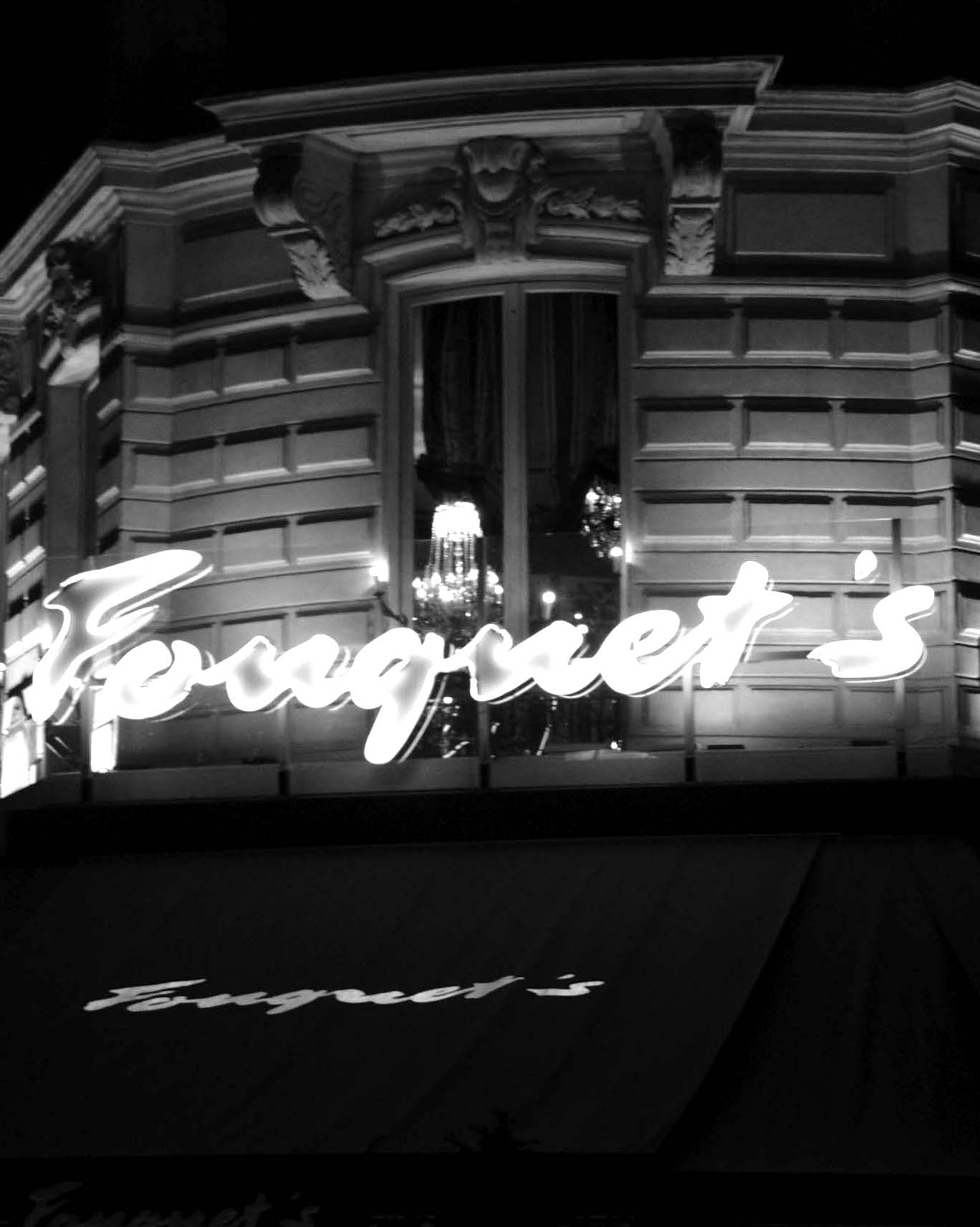 Fouquet’s neon script on a Haussmann façade with a chandelier behind