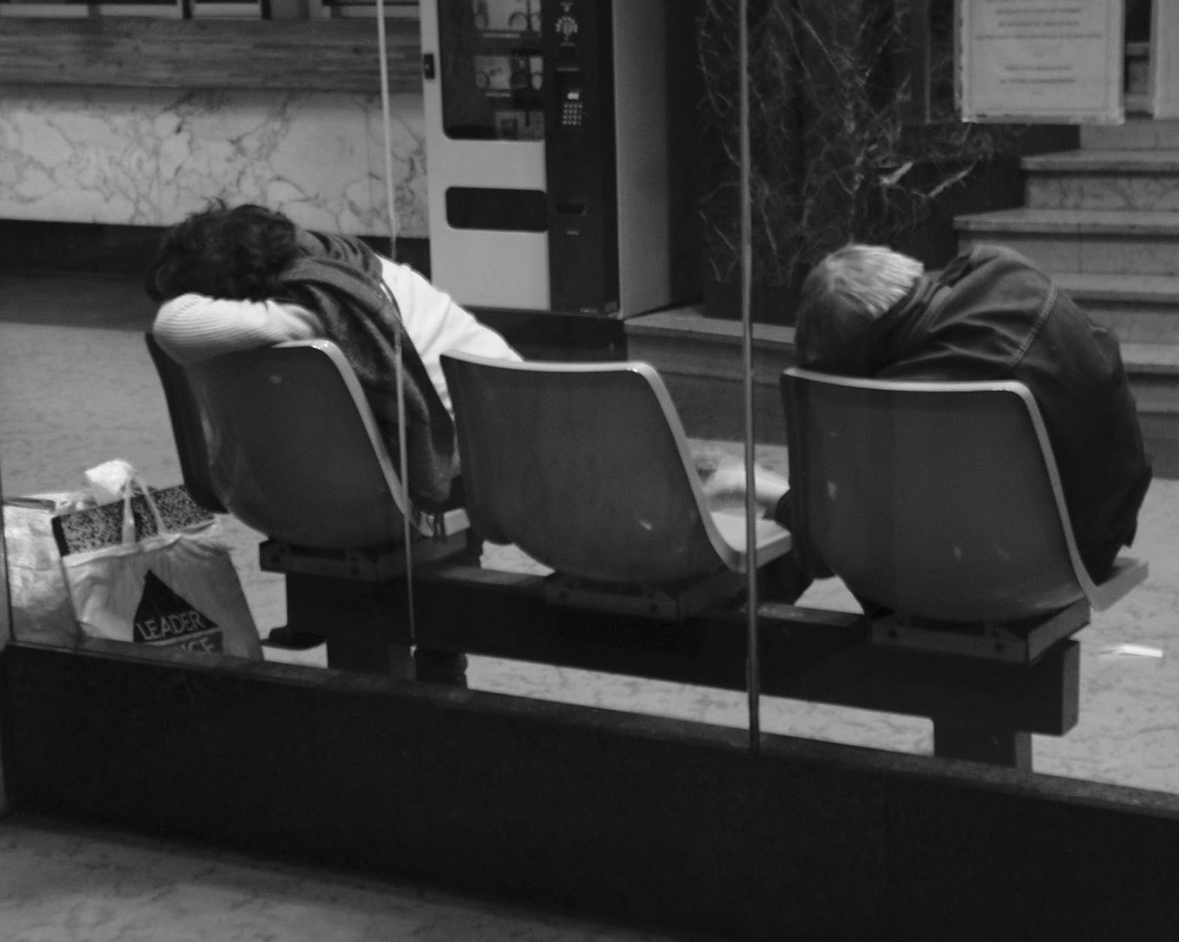 Two people asleep on plastic seats in a waiting hall