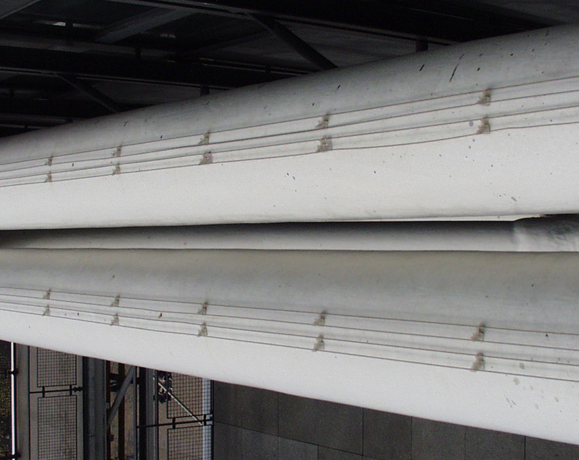 Long white pipes running along a building, seen from below