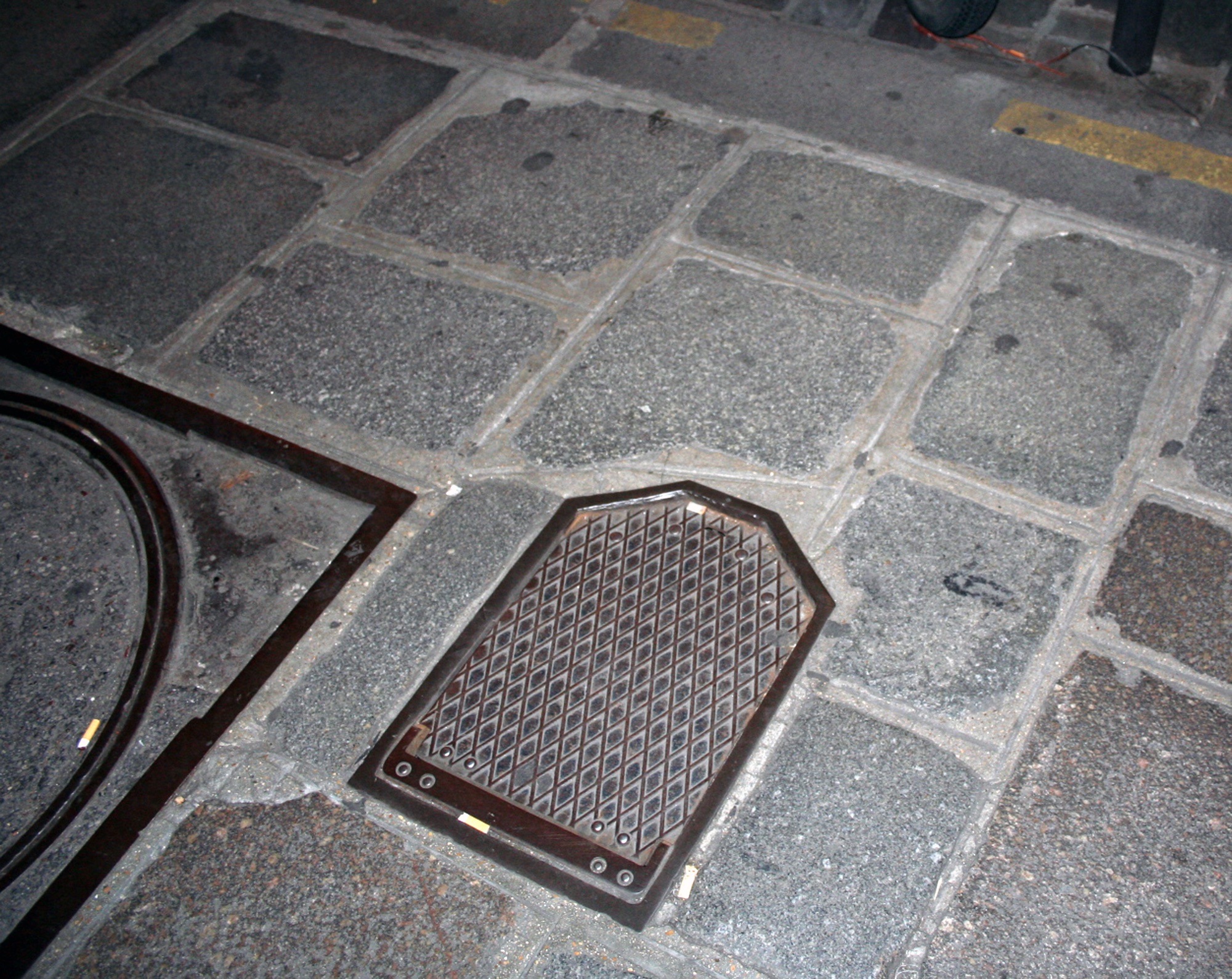 A metal drain cover set into grey paving stones