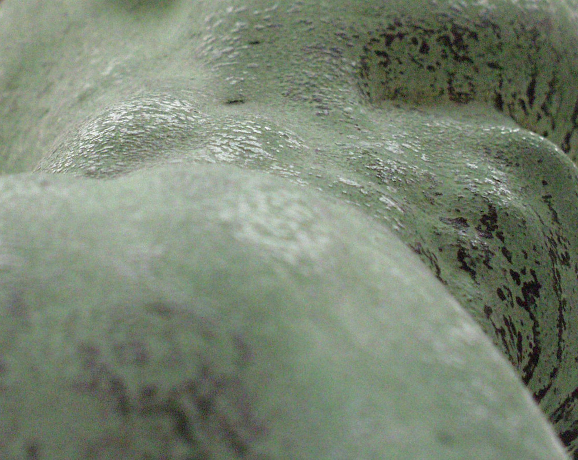 Close-up of a pale green statue, mottled with dark marks