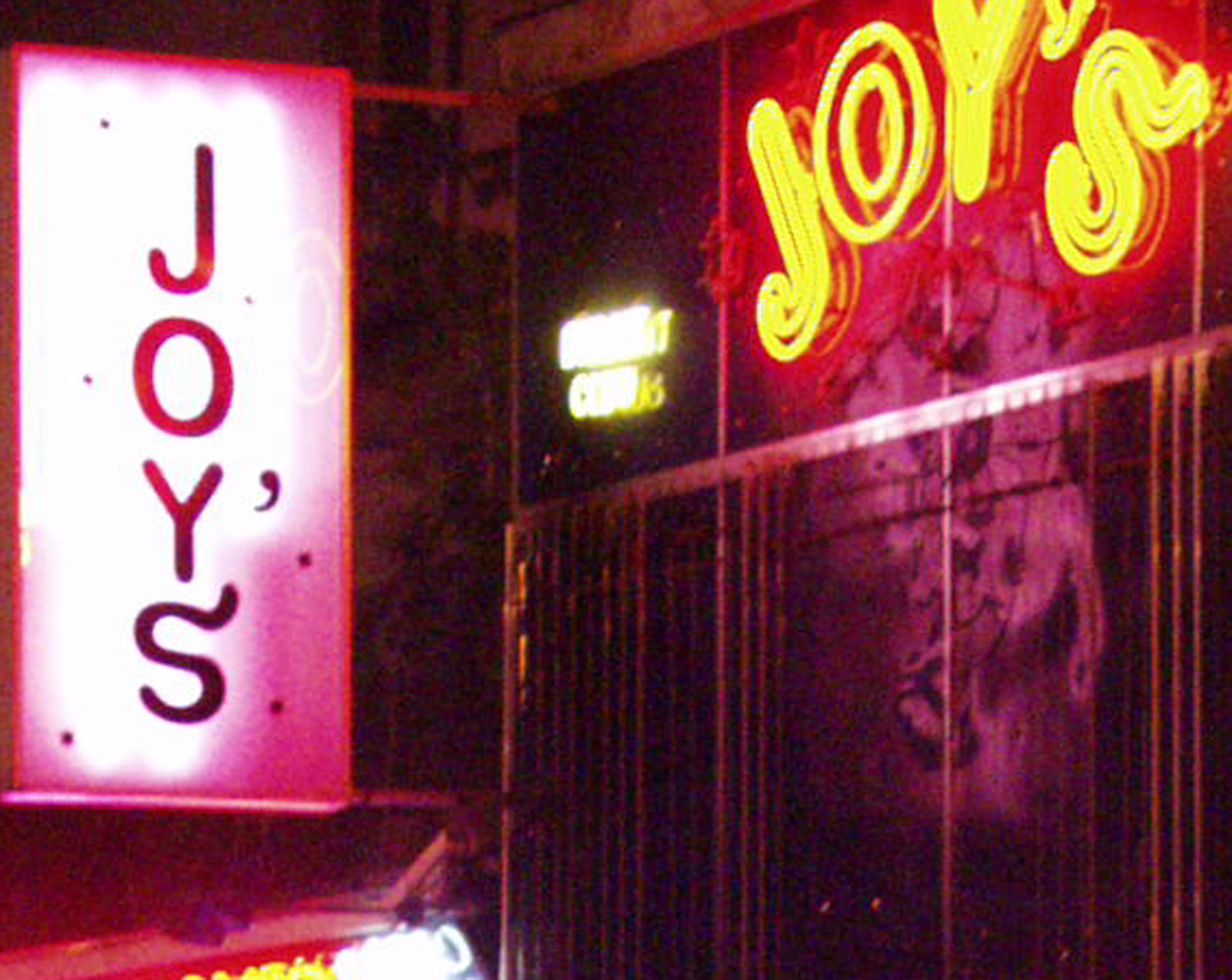 Neon sign reading Joy's in red and yellow on a dark wall