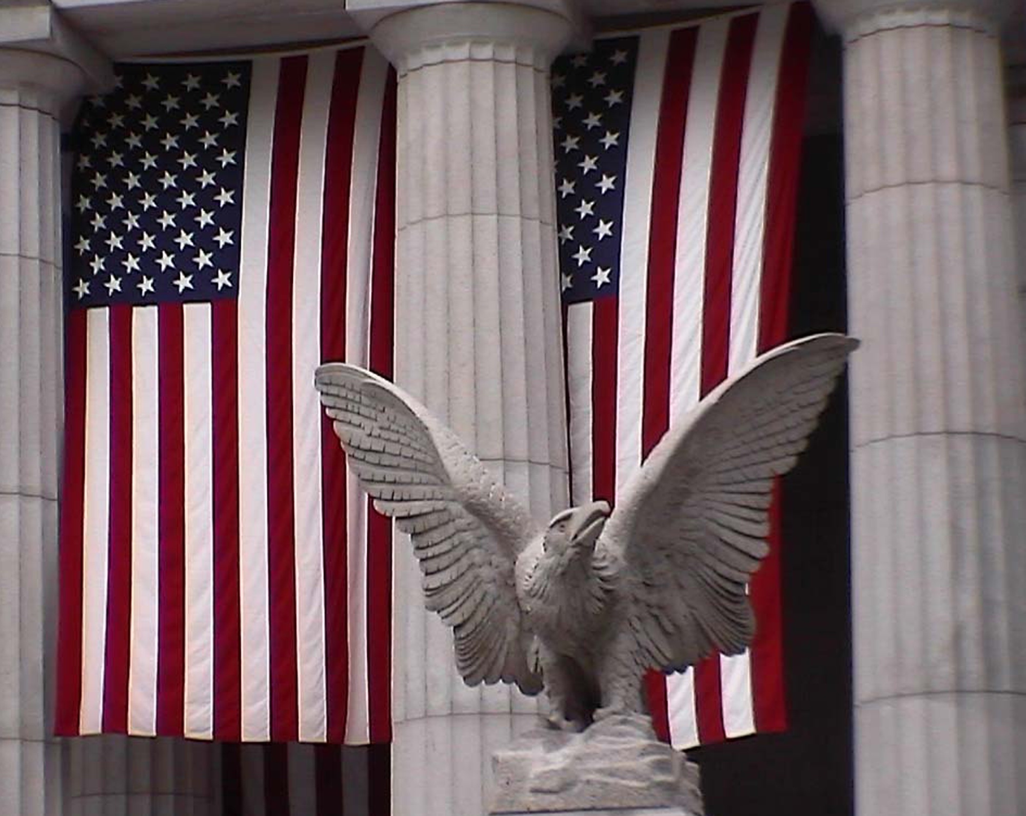 American flags hanging behind a stone eagle and columns