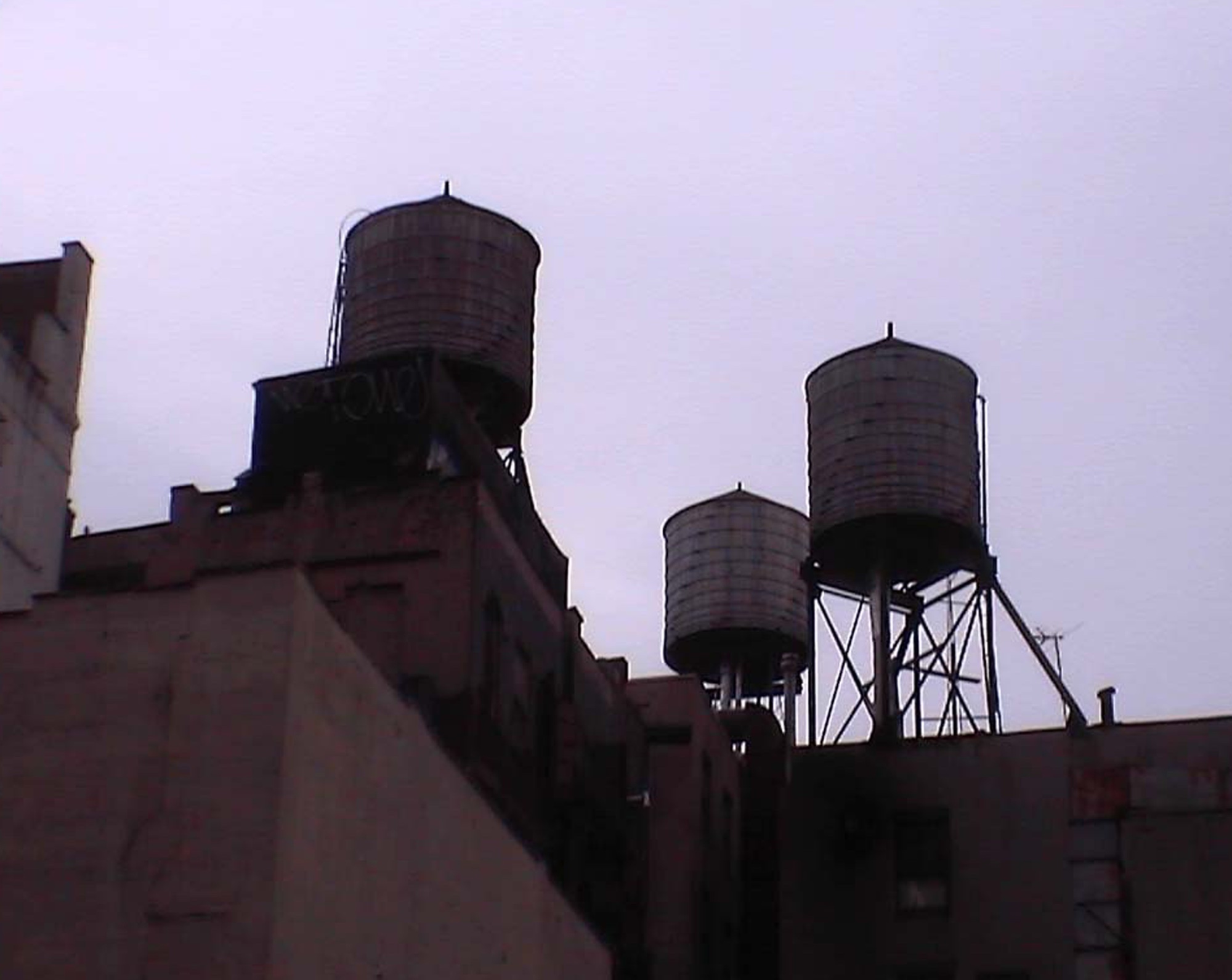 Three water towers on rooftops in violet evening light