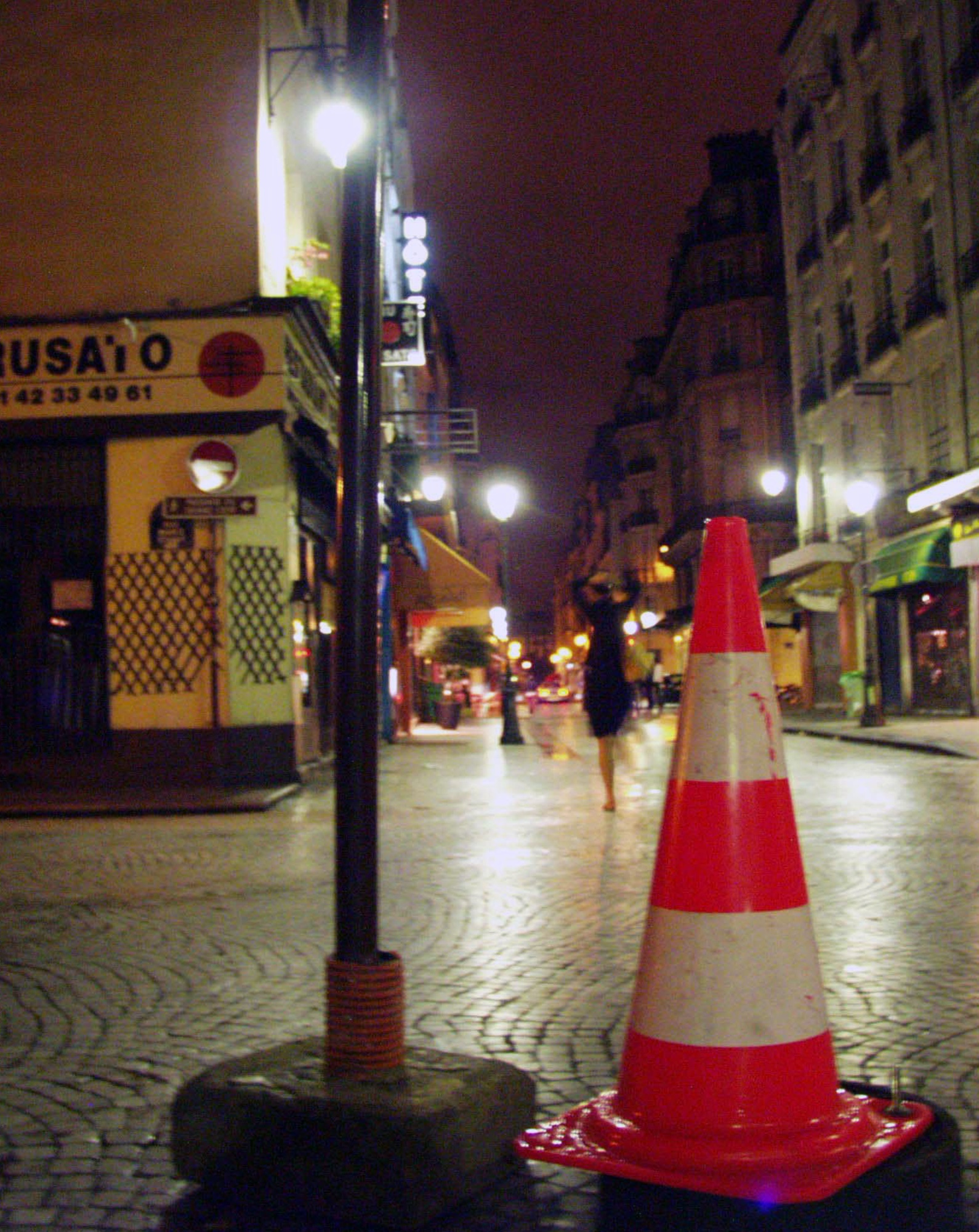 Wet cobbled street at night, a red and white traffic cone beside a lamp post