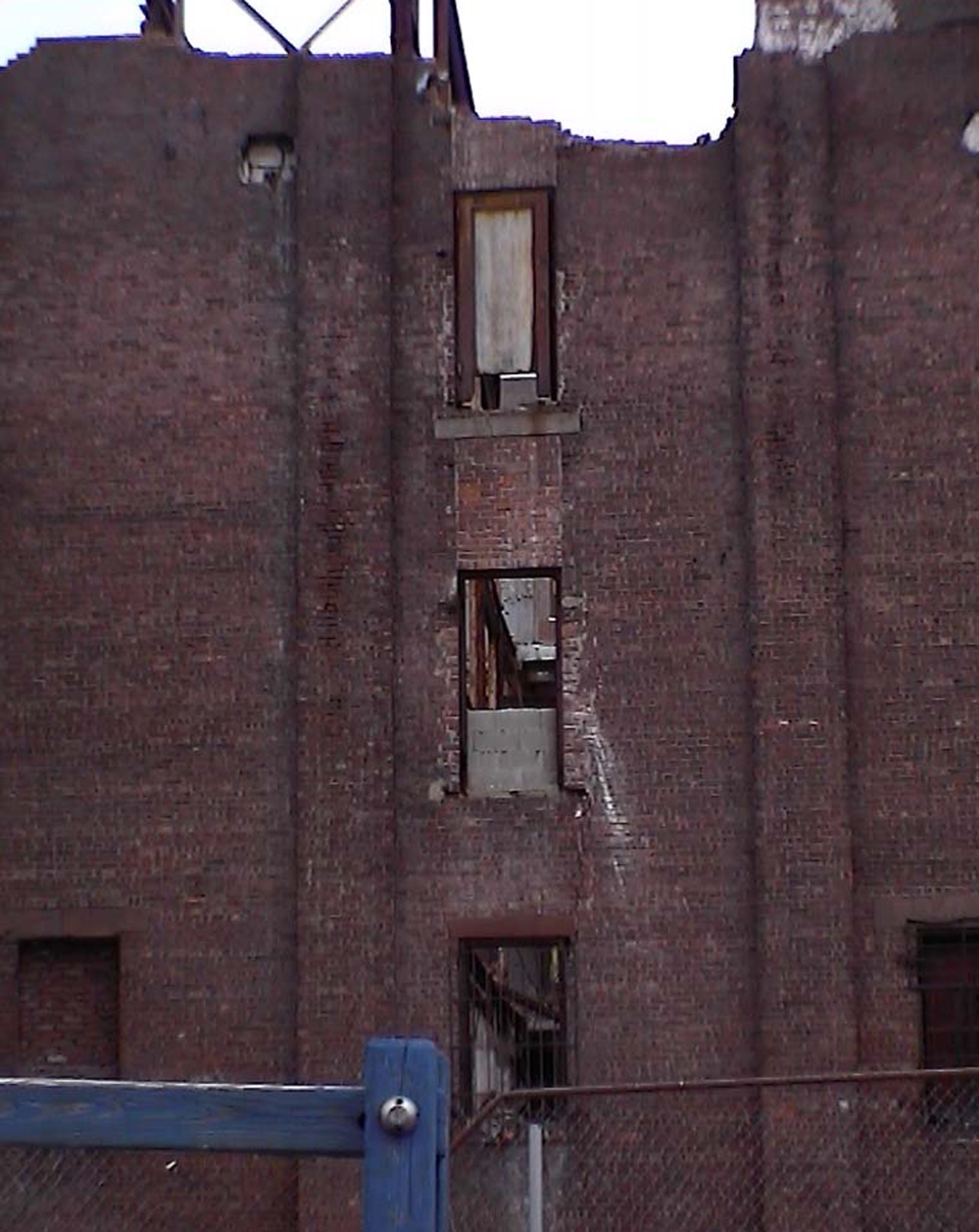 Brick tenement with broken windows behind a blue fence