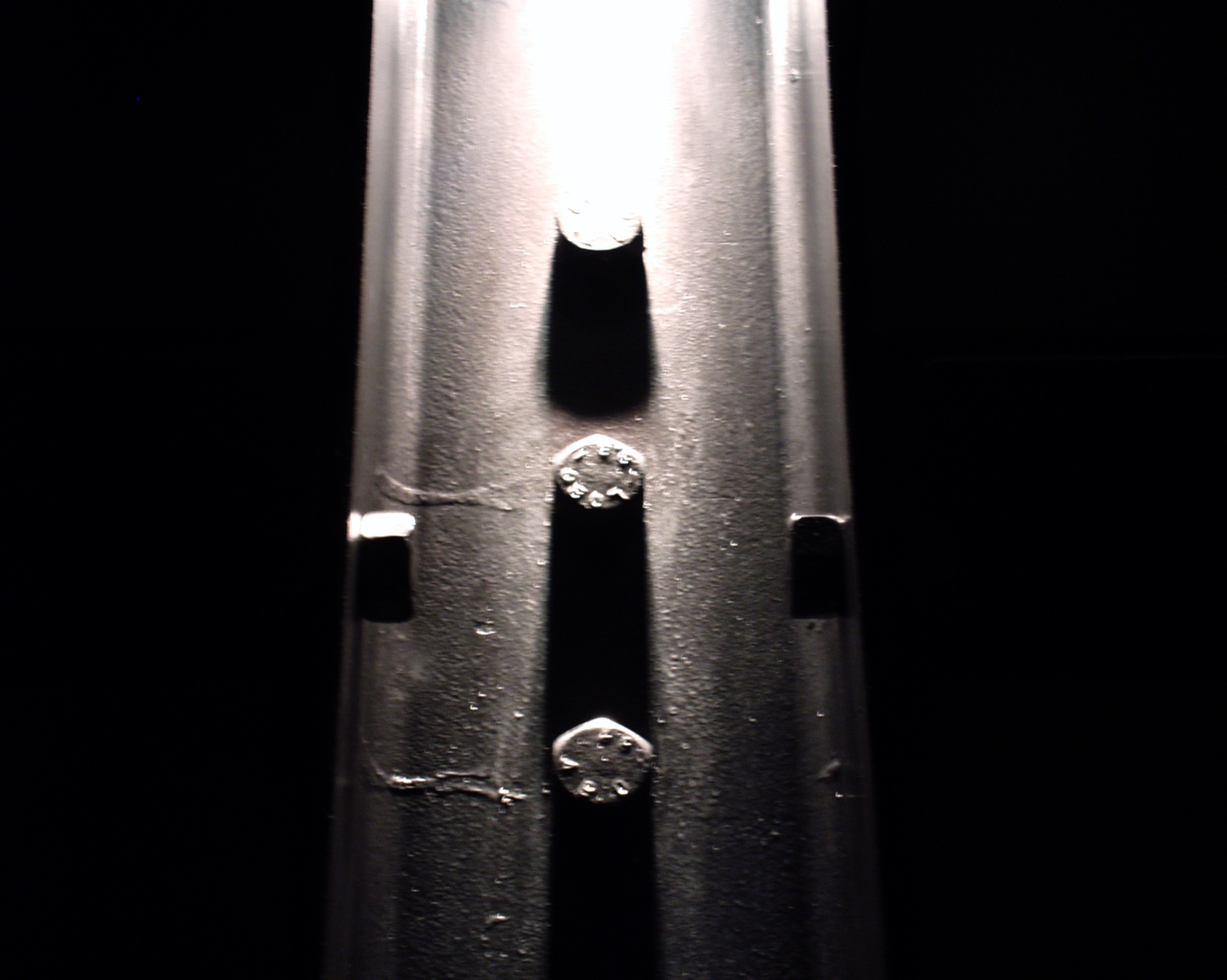 A steel pole lit from above against black