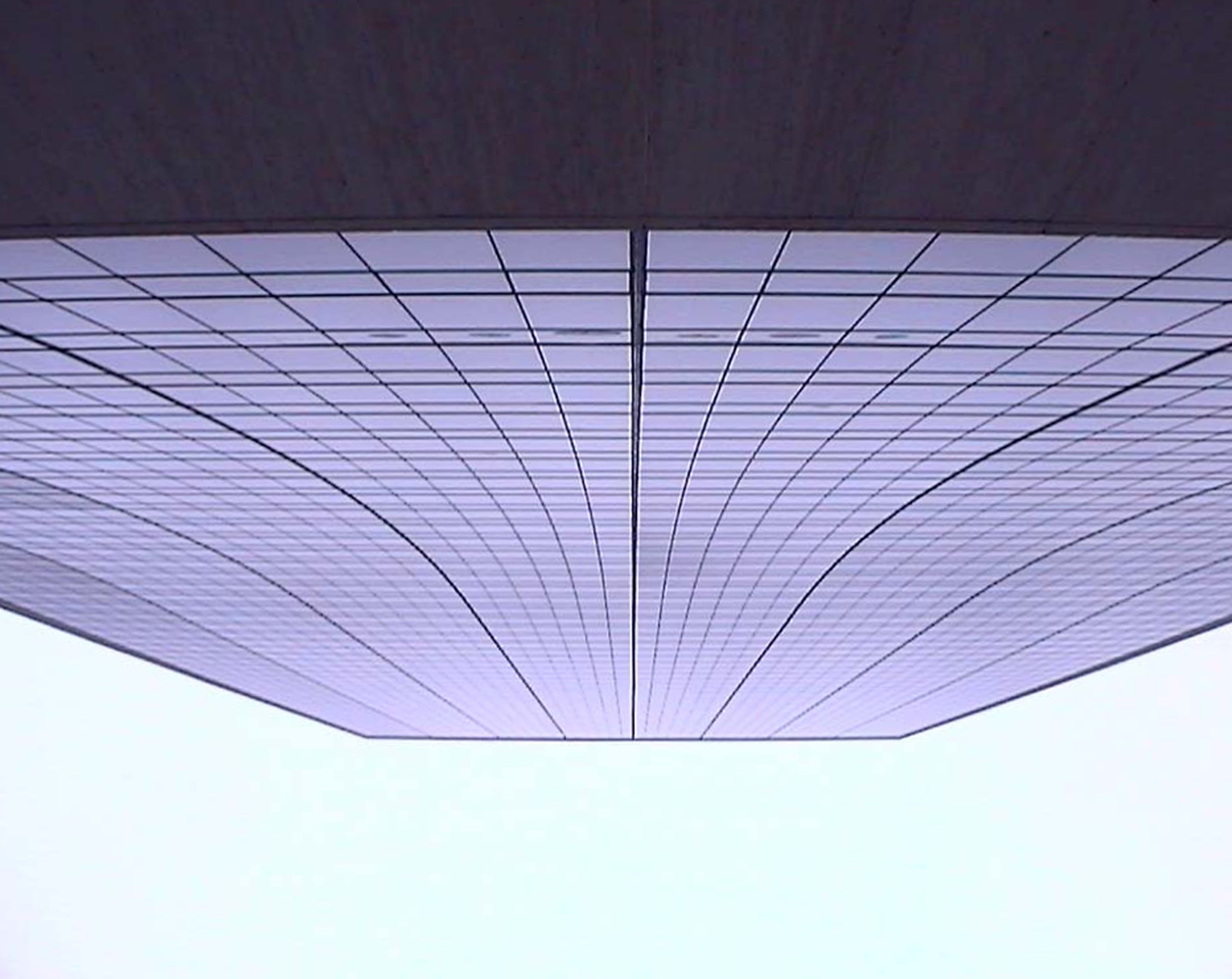 Underside of a tower's overhang, lines converging against a pale sky