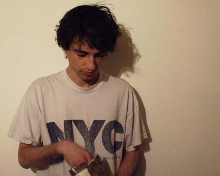 A young man in an NYC T-shirt against a pale wall, looking down into a paper bag