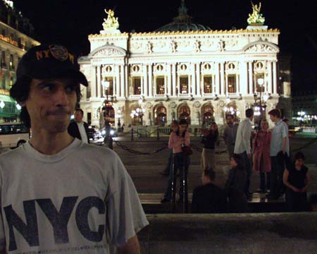 The young man in front of the lit Opéra Garnier, people on its steps