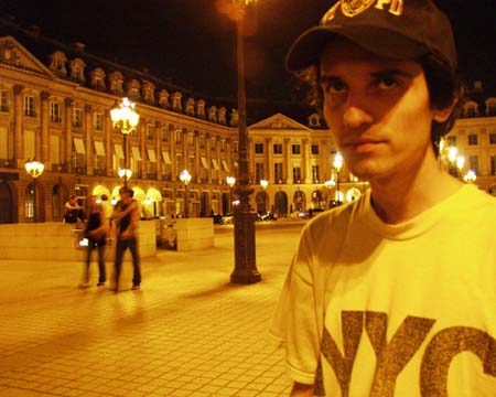 Close on the young man in Place Vendôme, the lit façades behind