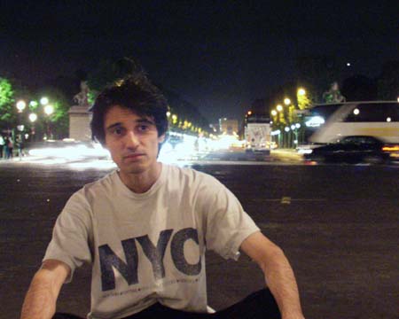 The young man sitting, shoulders down, the lit avenue behind him