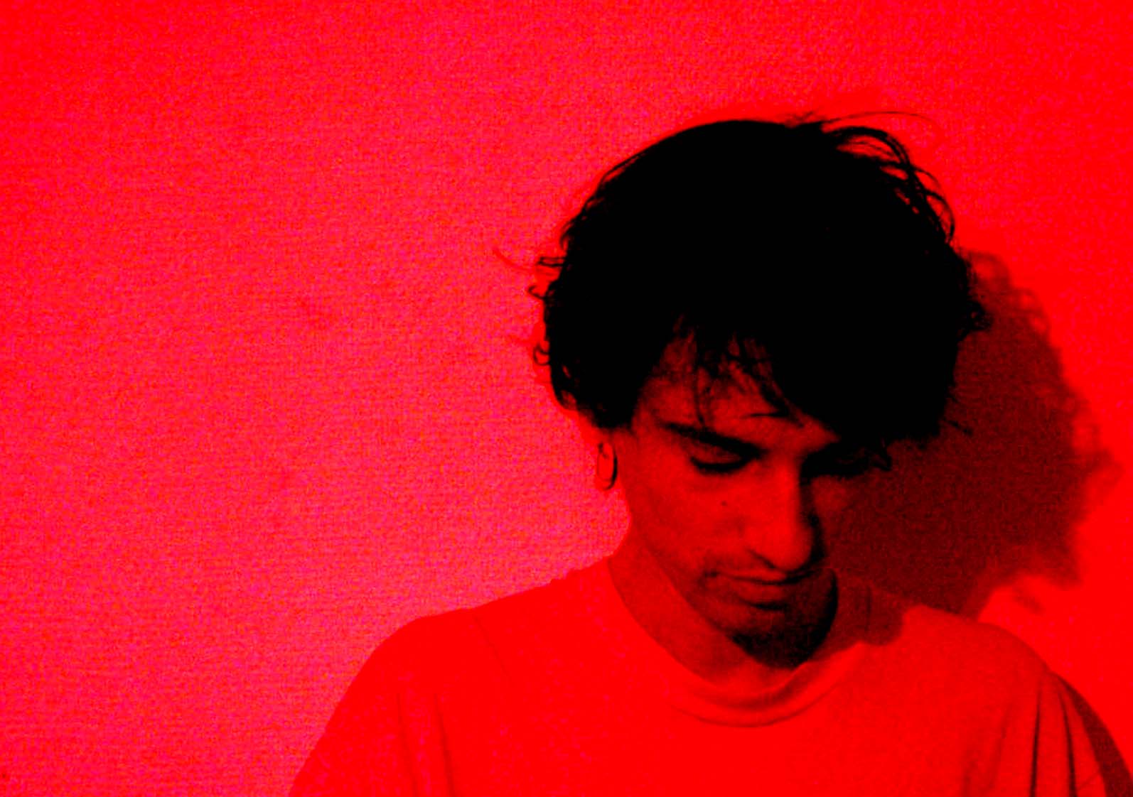 A man against a red wall, head bowed, his shadow behind