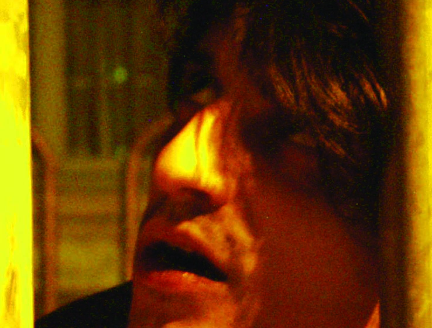 Close profile of a face pressed near a bright bar, mouth open