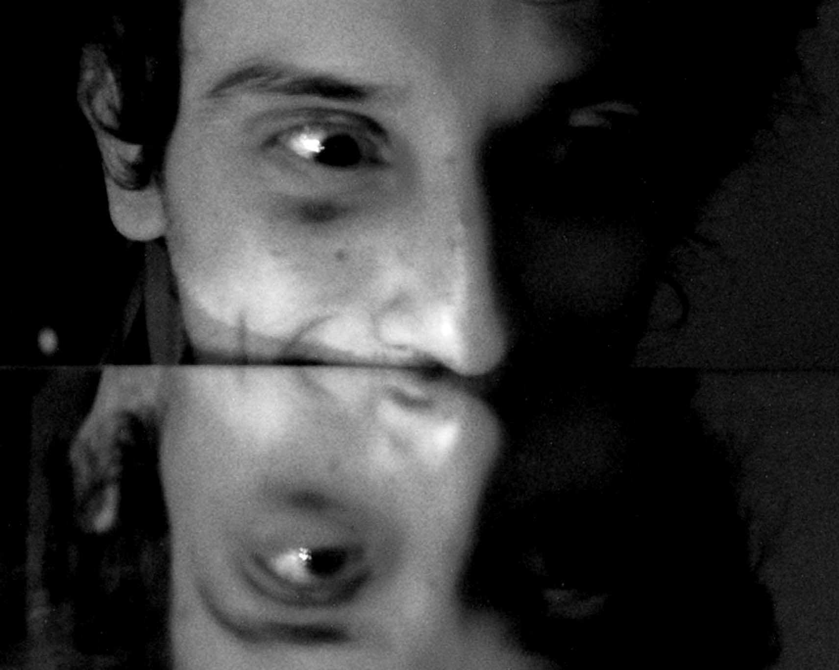 Half a face and its blurred reflection split by a mirror edge