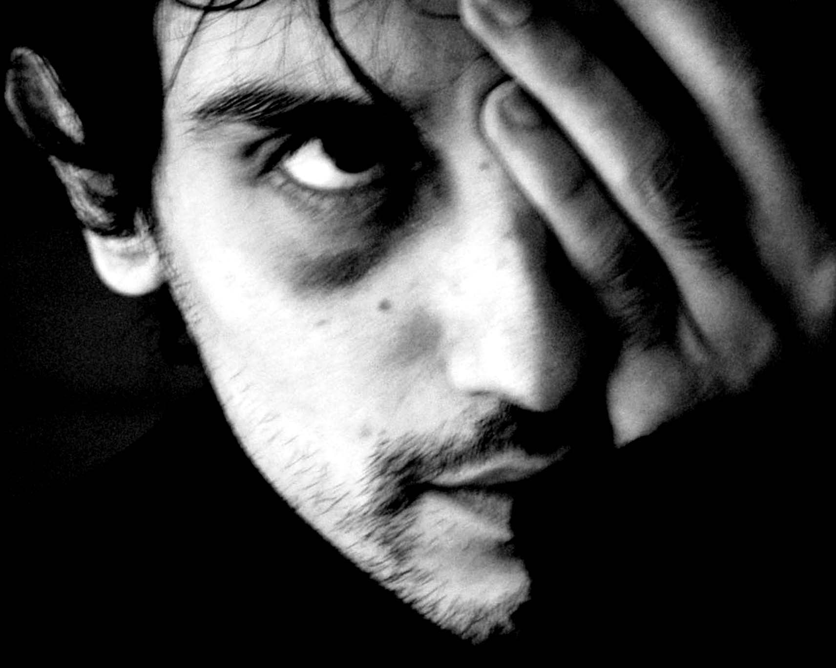 Face in deep shadow, one eye visible, a hand across the forehead