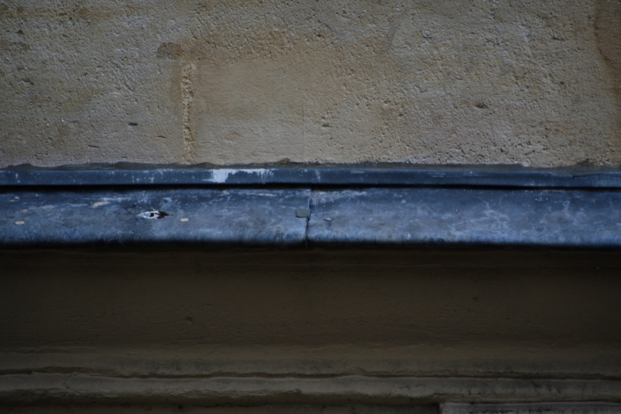 A blue gutter under a pale stone wall